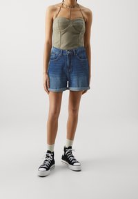 Olive green strapless top with seam details paired with denim shorts, light blue at the top, darkening towards the bottom, rolled cuffs, black sneakers.