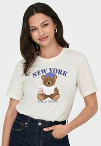 Cremefarvet bomulds t-shirt med et bjørnegrafik iført en blå hat og holder en pink drik, med teksten "NEW YORK City of Dreams".