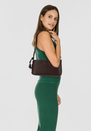 Borsa a mano in pelle marrone con forma strutturata, logo in rilievo, tracolla regolabile e finitura texturizzata. La modella posa indossando un vestito verde.