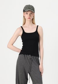 Svart tanktopp med firkantet utringning og tykke stropper, kombinert med grå og svarte stripete bukser med snor i livet.