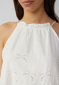 Weißes Baumwolloberteil mit gerafftem Ausschnitt und dünnen Trägern, verziert mit floralem Stickerei und Ausschnitten am Saum.