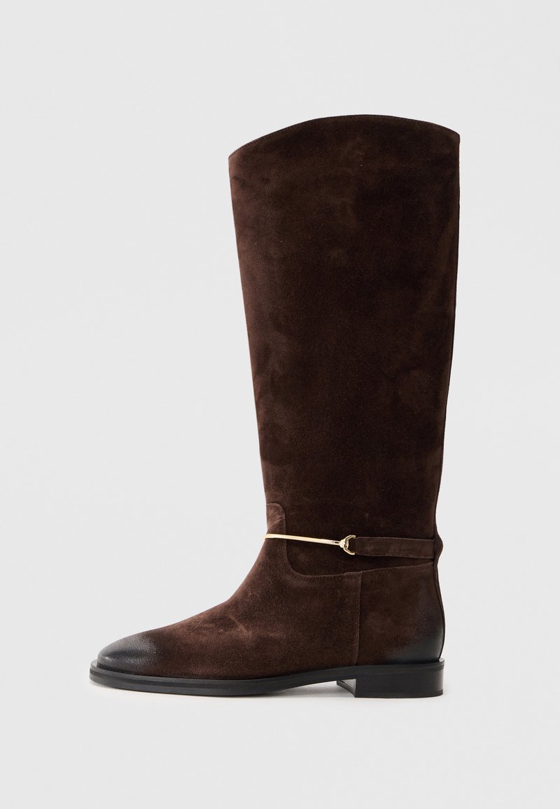 Hnědé nubukové kozačky do poloviny lýtek s kulatou špičkou, černým koženým lemem a zlatou ozdobnou páskou kolem kotníku. Hladká textura a strukturovaný tvar.