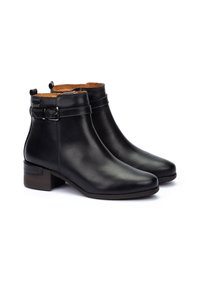 Botas de tobillo de cuero negro con un tacón bajo de bloque, que presentan un detalle de hebilla y una textura suave, con un forro marrón claro para el contraste.