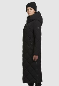 Abrigo largo negro tipo plumas con un patrón de rombos, capucha, bolsillos laterales con cremallera y gorro de punto acanalado. Textura suave, resistente al agua.