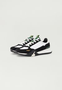 Zapatillas en blanco y negro con un diseño texturizado, detalles en verde y un logotipo. Cuentan con suelas gruesas y cordones en contraste.