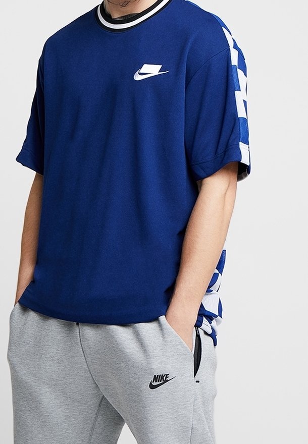 Námořnická modrá tričko s krátkým rukávem s bílým logem Nike na hrudi, s černobílým pruhovaným límcem a kostičkovanými modrými bočními akcenty.