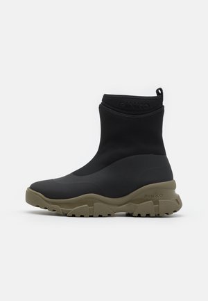 Bottes montantes noires avec une finition lisse et mate. Semelle en caoutchouc vert olive, dotée d'une texture antidérapante. Logo estampé sur le talon.