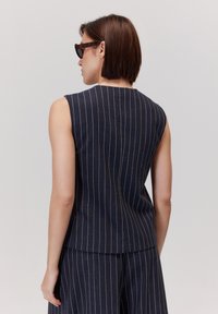 Granatowy top bez rękawów w pionowe złote prążki, z dopasowanym krojem i okrągłym dekoltem, pokazany z tyłu.