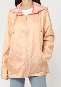 Chaqueta ligera rosa con un patrón de manchas, cierre completo y capucha ajustable. Presenta bolsillos laterales y una textura suave.