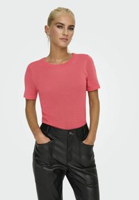 Suéter de coral de manga corta y cuello redondo, hecho de una tela de punto suave, combinado con pantalones de cuero negros de tiro alto con grandes bolsillos.