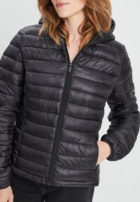 Giacca a vento nera con cappuccio, dotata di sezioni trapuntate, cerniera frontale e polsini elasticizzati. Leggera, con una texture liscia.