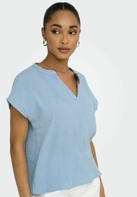 Lys blå, struktureret bluse med V-hals og korte ærmer. Stoffet har et subtilt krøllede mønster, der giver en afslappet pasform.