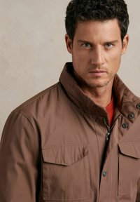 Brązowa, ocieplana kurtka z wysokim kołnierzem, zamek błyskawiczny z przodu i dwie kieszenie na klatce piersiowej. Charakteryzuje się gładką teksturą i zatrzaskami.