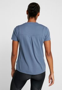 Sportovní tričko s krátkými rukávy v světle modré barvě s texturovanou látkou, rozděleným zadním dílem a jemnými tečkovanými akcenty na zadní části.