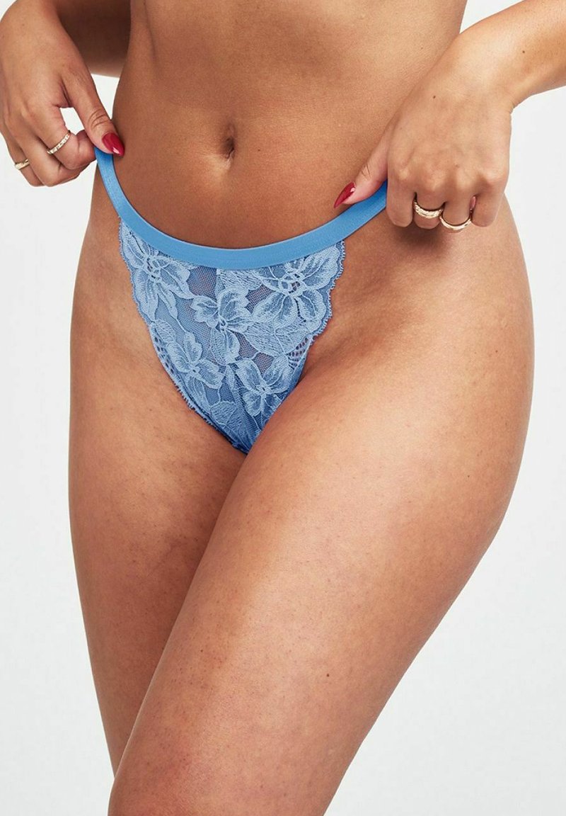 Ljust blå spets-tanga med blommönster, med en kontrasterande enfärgad blå midja. Tyget har ett genomskinligt, texturerat utseende.
