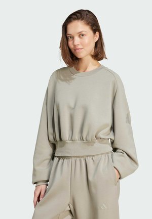 Felpa beige chiaro con orlo inferiore arriccicato, maniche lunghe, collo rotondo e sottili dettagli del logo sulle maniche. Tessuto morbido.