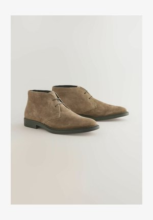 Ruske nahkasaappaat nilkkoihin, pyöreällä kärjellä, vähäisellä ompelulla ja mustalla kumipohjalla. Ominaisuuksiin kuuluu yksinkertainen nauhakiinnitys.