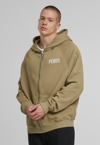Olive green zip-up hoodie with white text “PEQUS,” featuring a relaxed fit, ribbed cuffs, and front pockets. Cotton blend material.