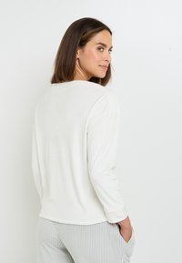 Top bianco a maniche lunghe con scollatura rotonda, in morbido cotone, vestibilità rilassata e orlo curvo, abbinato a pantaloni a righe.