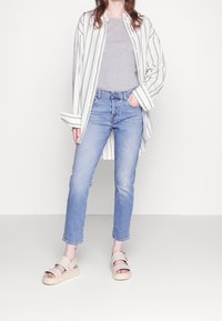 Pruhovaná košile na knoflíky v krémové a námořnické barvě, šedé tričko, světle modré skinny jeans a béžové sandály na platformě se strapcovým detailem.