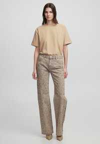 Camiseta beige de manga corta combinada con pantalones de tiro alto de color marrón claro con un patrón moteado; modelo vistiendo zapatos puntiagudos dorados.
