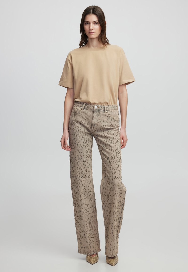Camiseta beige de manga corta combinada con pantalones de tiro alto de color marrón claro con un patrón moteado; modelo vistiendo zapatos puntiagudos dorados.