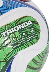 Nogometna lopta s bijelom podlogom, zelenim i plavim geometrijskim uzorcima, zlatnim akcentima i brendiranjem na više jezika.