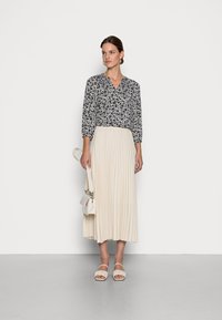Blusa azul marinho com padrão floral, decote em V e mangas três quartos, combinada com uma saia midi plissada em creme. Sandálias de salto bloco brancas e bolsa.