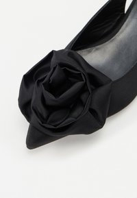 Črne slingback čevlje z ostrim nosom in velikim cvetnim detajlom iz blaga spredaj, z gladko satensko teksturo in mat končno obdelavo.