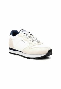 Sneaker bianca e beige realizzata in suede e materiali sintetici, con una suola testurizzata, accenti blu navy e branding stampato sui lacci.