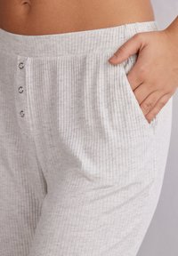 Lichtgrijze, geribde broek met een zachte textuur, voorzien van een brede elastische tailleband en decoratieve metalen knopen bij de zak.