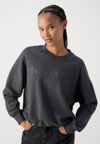 Felpa grigia carbone con collo a girocollo, caratterizzata da un logo "Marc O'Polo" in rilievo sulla parte anteriore. Tessuto morbido, vestibilità rilassata, maniche lunghe.