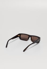 Gafas de sol de carey rectangulares con lentes tintados en marrón y el logo "vogue" en dorado en la patilla, exhibidas sobre un fondo blanco.