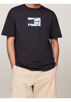 Sort bomuld T-shirt med en centreret hvid og grøn grafik med teksten "TOMMY JEANS." Kortærmet med rund hals.