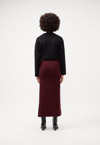 Fekete hosszúujjú felső, amelyhez egy illeszkedő bordó szoknya párosul; sima textúra, minimalista dizájn és elegáns fekete bokacsizma.