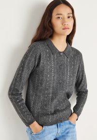 Grijze gebreide cardigan met verticale ribbels en subtiele pailletten details. Voorzien van een kraag en zes knopen aan de voorkant.