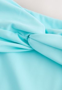 Tissu bleu clair lisse, plié et torsadé, montrant une texture douce et de délicats plis sur un fond neutre.