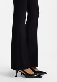 Black patent leather slingback heels with a pointed toe and a 2-inch kitten heel. Smooth texture with a glossy finish and minimalist design.