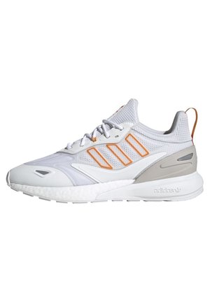Baskets de sport blanches et gris clair avec dessus en mesh à rayures orange, lacets blancs et semelle amortissante, vue latérale.