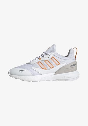 Zapatilla deportiva blanca y gris claro con empeine de malla a rayas naranjas, cordones blancos y suela acolchada, vista lateral.