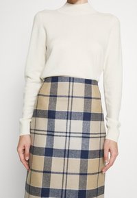 Licht crèmekleurige trui met hoge hals gecombineerd met een beige geruite rok met marineblauwe en lichtbruine vierkanten, geborstelde textuur en een nauwsluitend ontwerp.