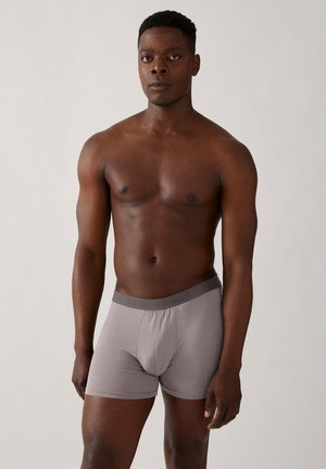 Grijze katoenen boxershorts met een gestructureerde tailleband met reliëflogo. Model staat blootsvoets in een neutrale houding.