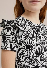 Vit ribbad topp med svart blommönster, med volangärmar och rund halsringning. Designen inkluderar olika blomformer och detaljer.