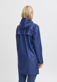 Impermeabile blu navy con cappuccio, caratterizzato da un design con yoke posteriore e maniche lunghe. Texture liscia e lucida, che arriva a metà coscia.