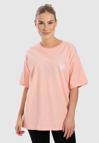 Camiseta de algodón rosa con mangas cortas, escote redondo y un pequeño gráfico de mariposa en el pecho. La camiseta tiene un ajuste relajado.