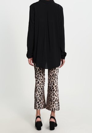 Osoba ubrana w czarną, długorękawową koszulę, krótkie spodnie w panterkę i czarne sandały na wysokim obcasie, stojąca tyłem.