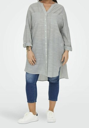 Overhemd met knopen in lichtgrijs met dunne witte strepen, lange mouwen en een afgeronde zoom, gecombineerd met skinny jeans en witte sneakers.