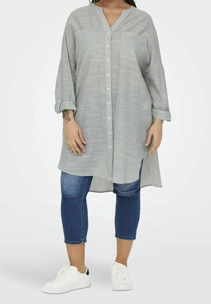 Chemise boutonnée gris clair avec fines rayures blanches, manches longues et ourlet incurvé, associée à un jean skinny et des baskets blanches.