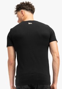 Juodas trumpas rankovė t-shirt, pagamintas iš medvilnės, su mažu auksiniu liūto logotipu ant nugaros ir klasikinio apvalaus kaklo dizainu.