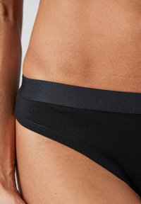 Zwarte bikinionderkant met een soepele, elastische tailleband, gestikte randen en een minimalistisch ontwerp. De stof heeft een zachte textuur.